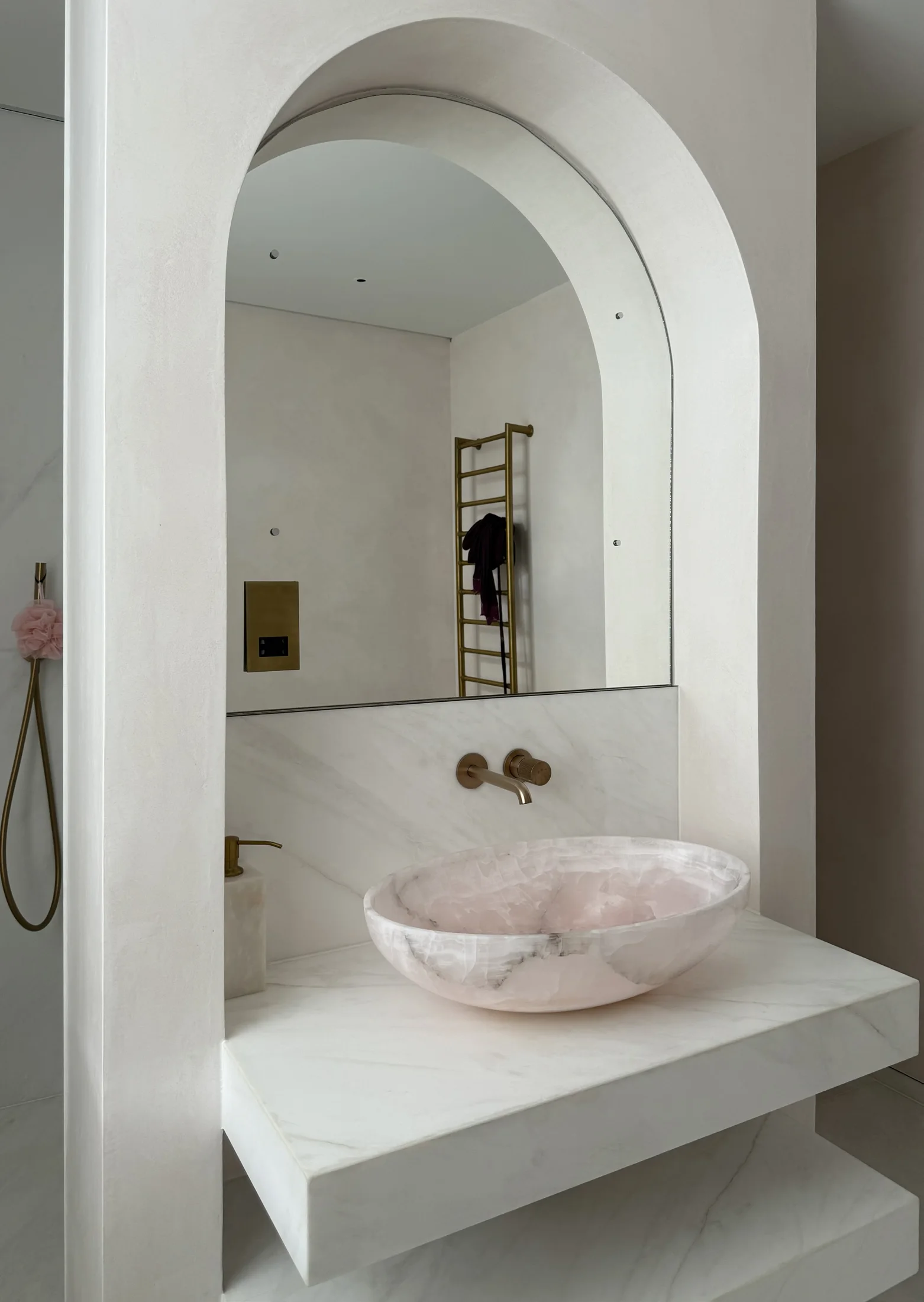 Pale stone bathroom with an arched vanity mirror