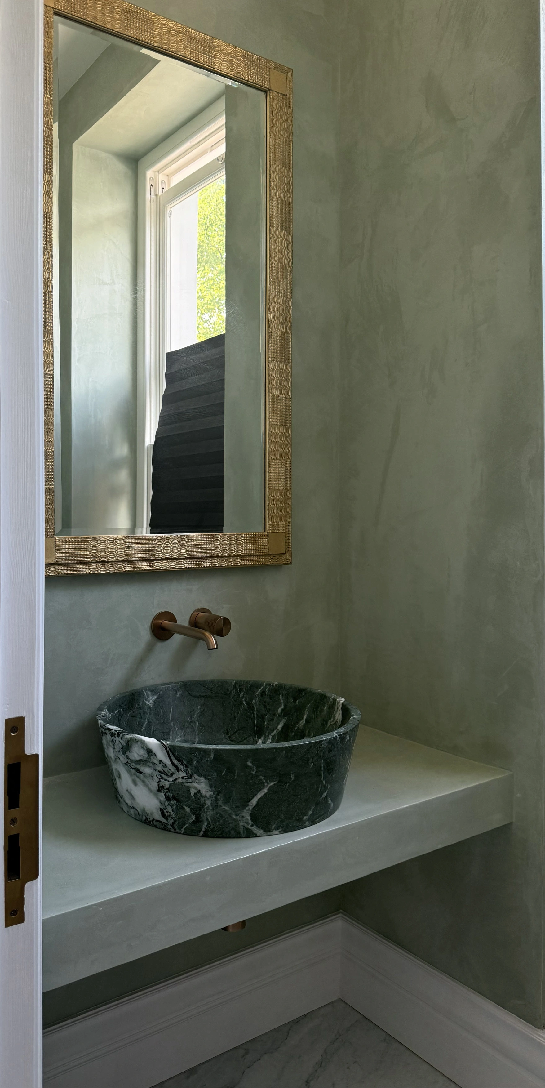 Powder room with green Venetian-plaster walls, a framed mirror, wall-mounted brass taps and a dark green marble vessel basin.