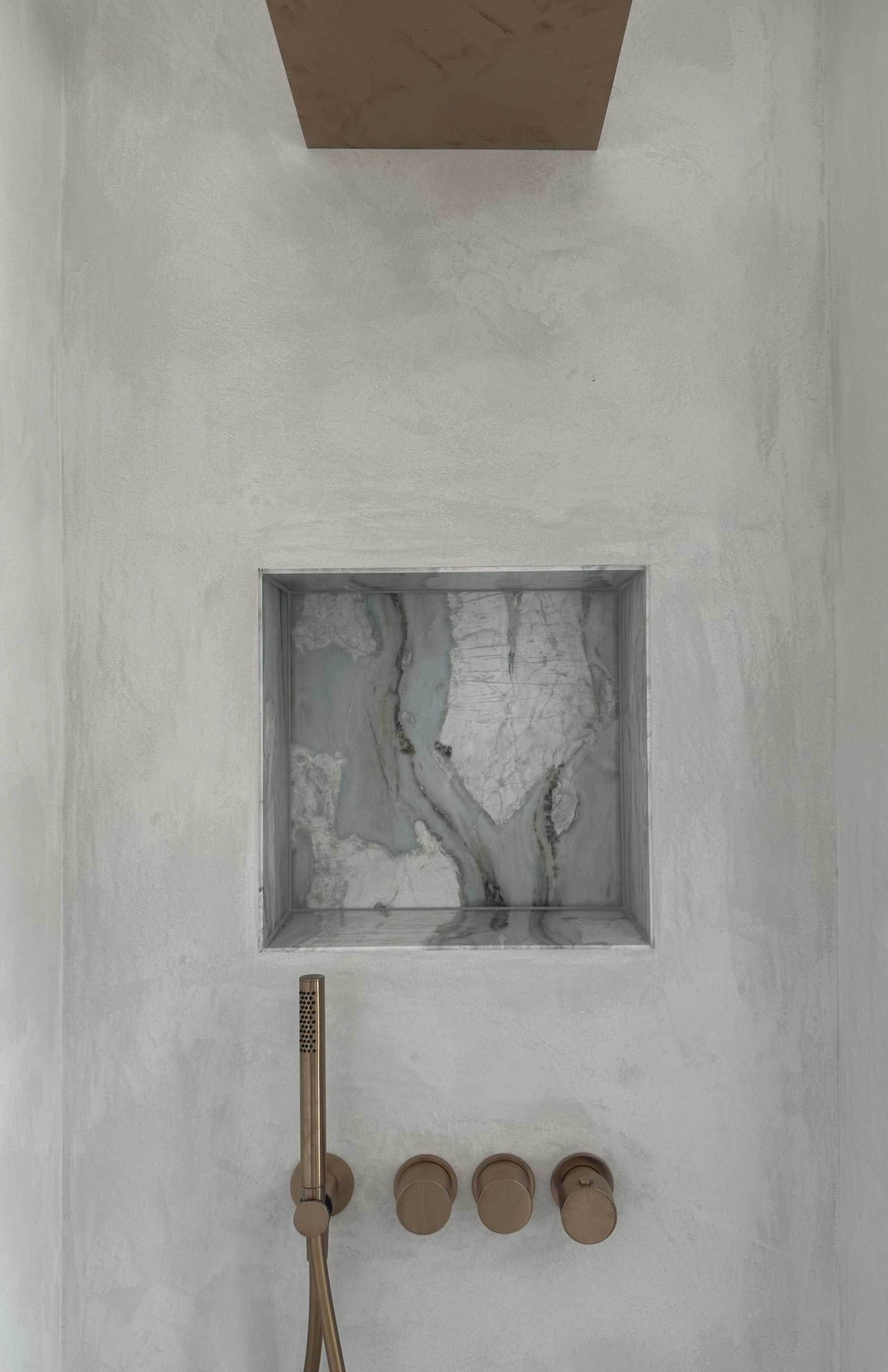 Venetian-plaster shower wall with a recessed book-matched marble niche and brushed-brass controls and hand shower.